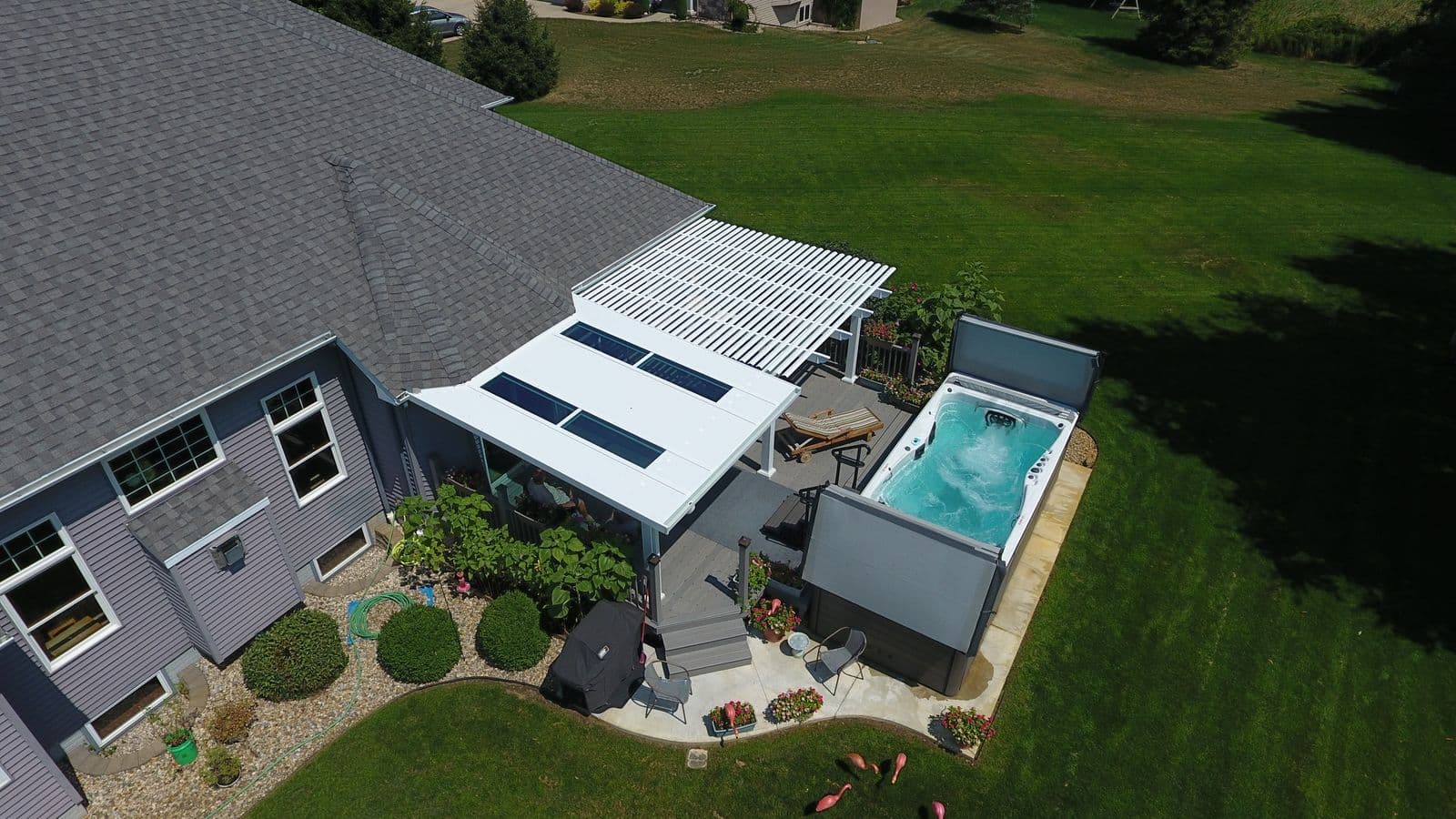 An aerial view of a gray deck with q white pergola and a hot tub.